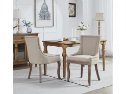 Juego de 2 sillas beige con patas de madera curvadas y ribete de tachuelas.